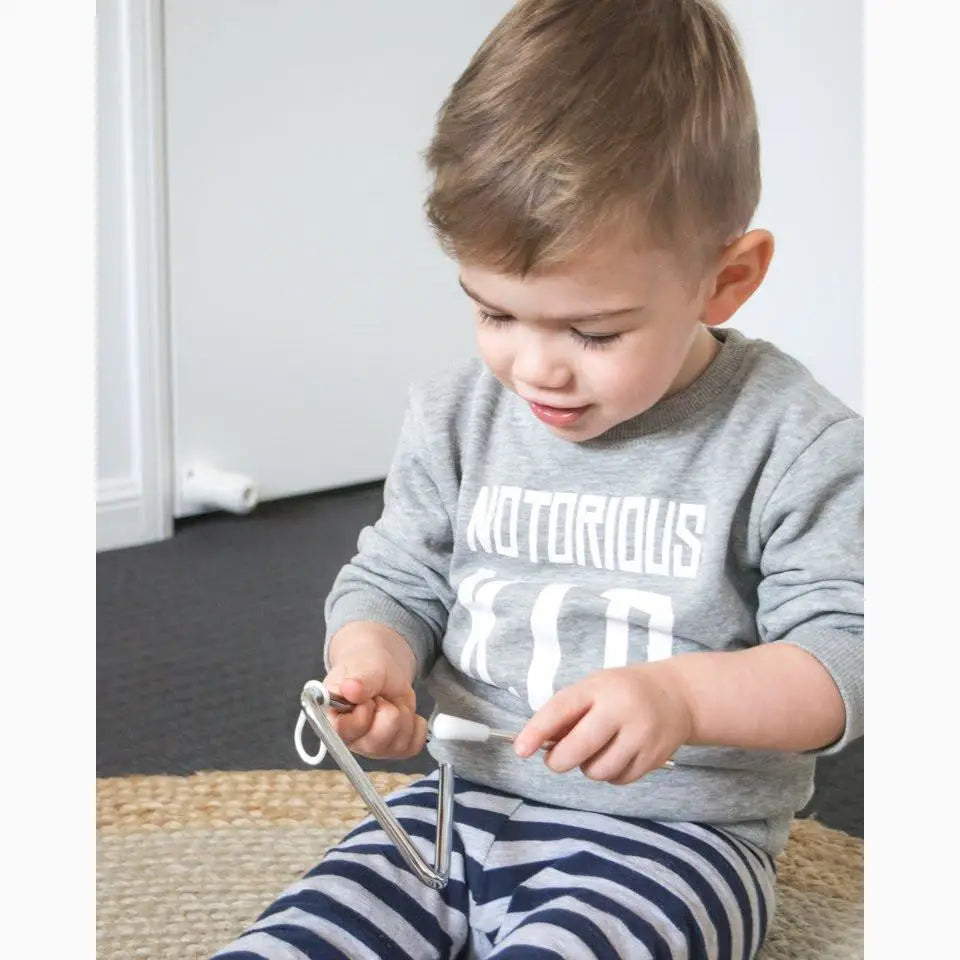 Young child wearing a gray sweatshirt and striped pants, sitting on the floor while looking down at something in their hands.