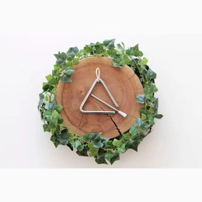 Triangle-shaped musical instrument on a wooden disc surrounded by green ivy leaves.