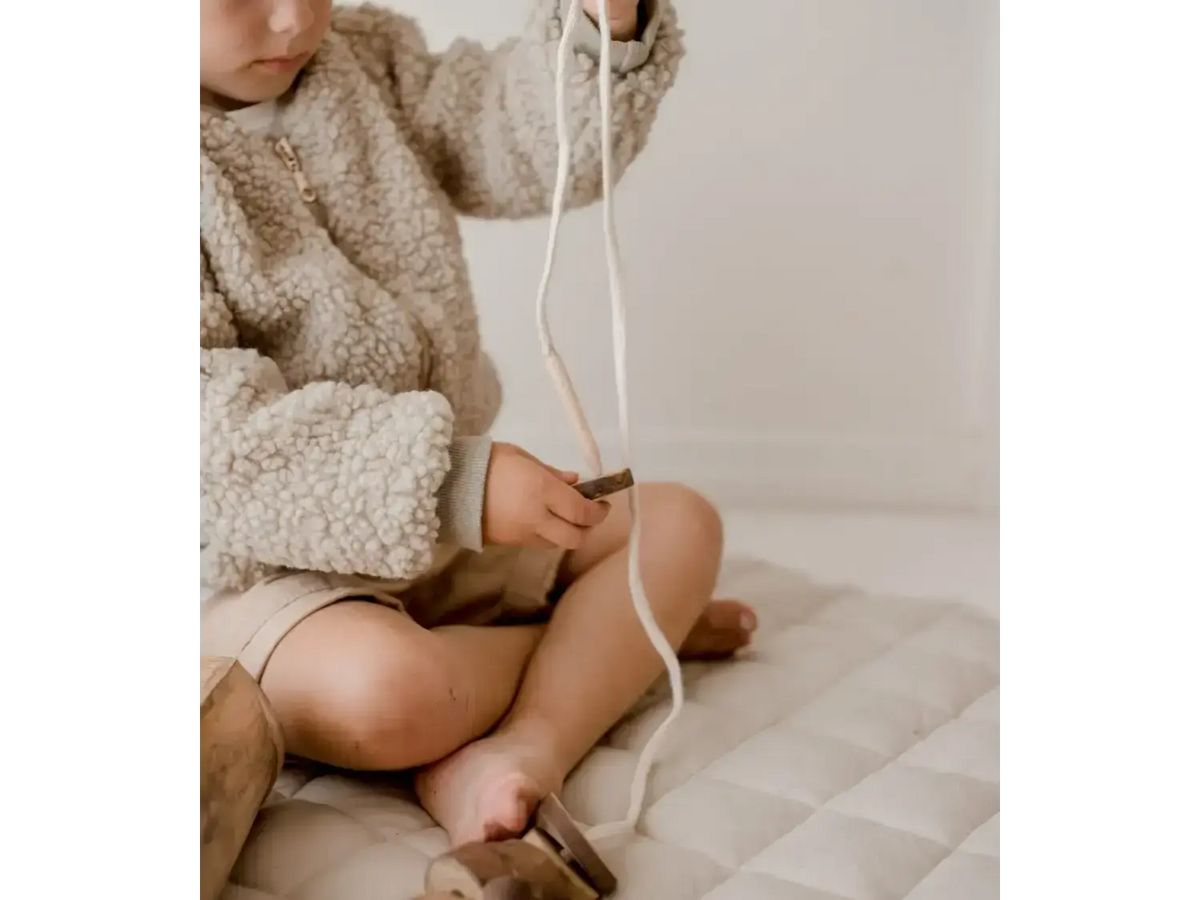 Child wearing a fluffy sweater playing with a string or rope.