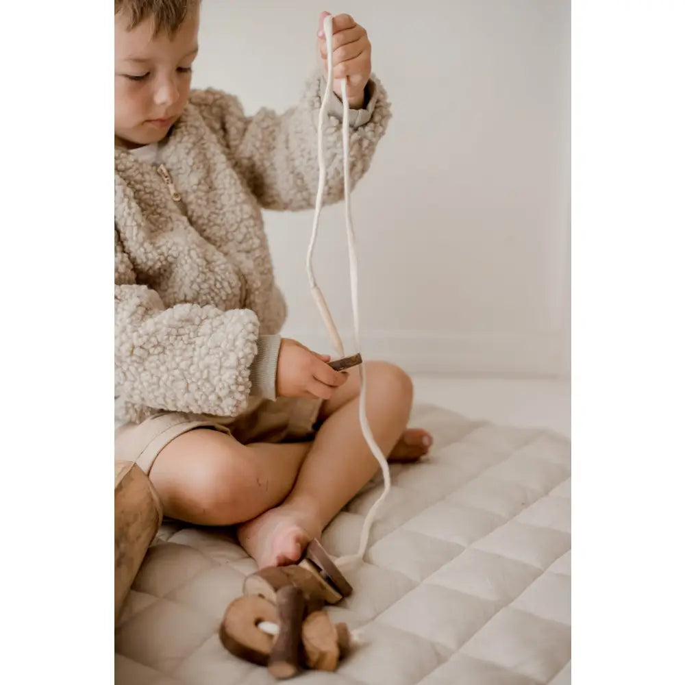 Child wearing a fluffy sweater playing with a string or rope.