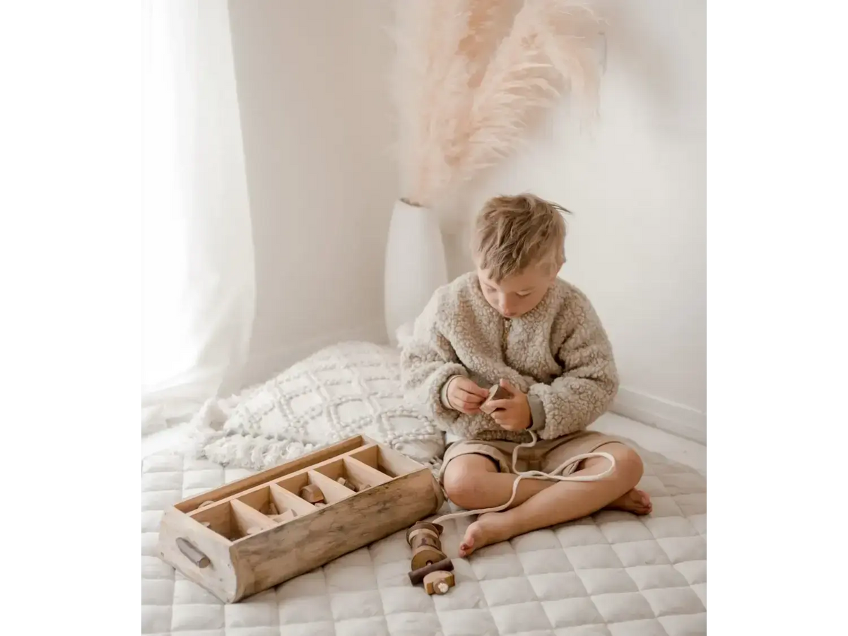 Child sitting cross-legged on a quilted surface, wearing a cozy sweater.