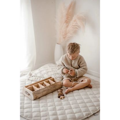 Child sitting cross-legged on a quilted surface, wearing a cozy sweater.