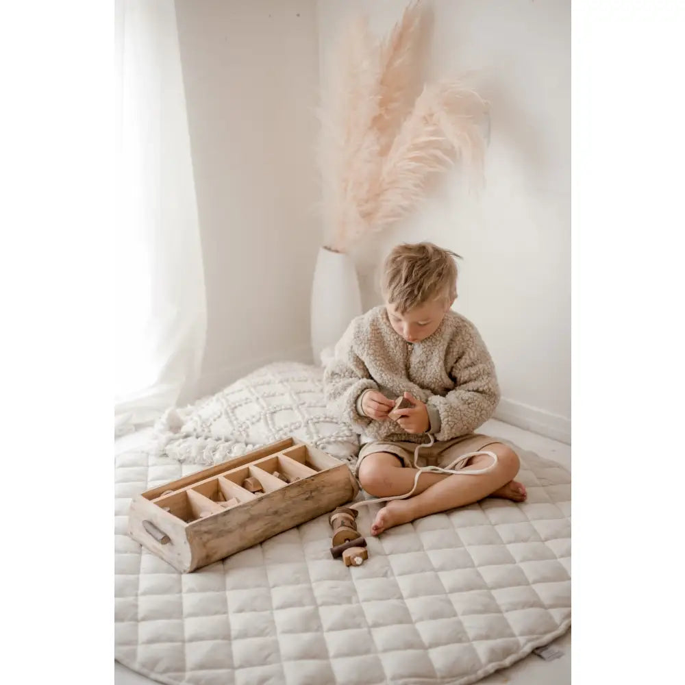 Child sitting cross-legged on a quilted surface, wearing a cozy sweater.