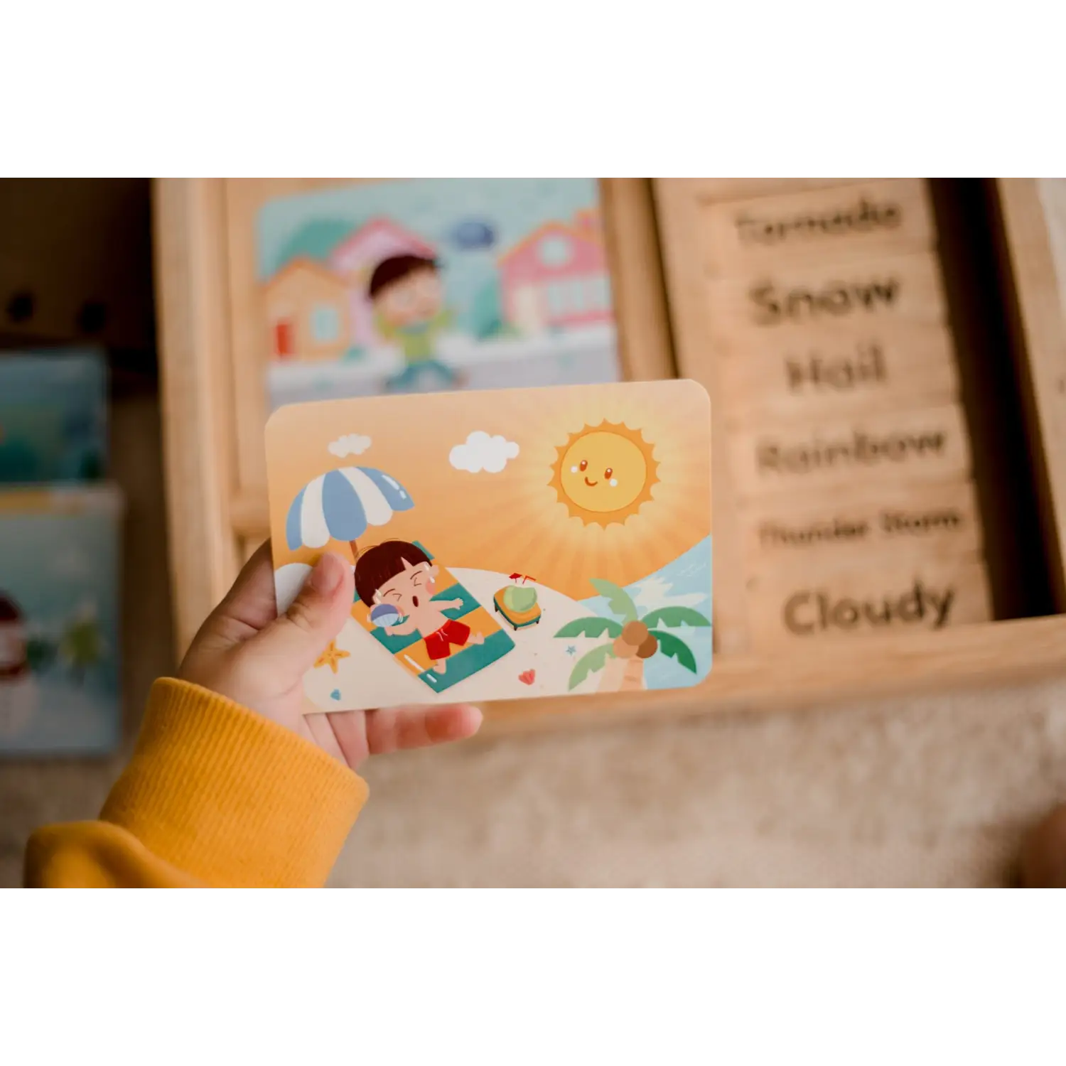 Colorful wooden card depicting a beach scene with a smiling sun and a child relaxing under an umbrella.