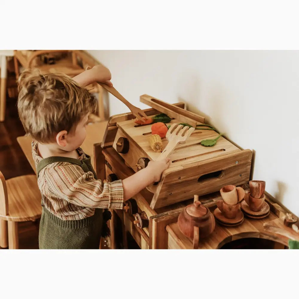 Wooden play kitchen with toy food and utensils.