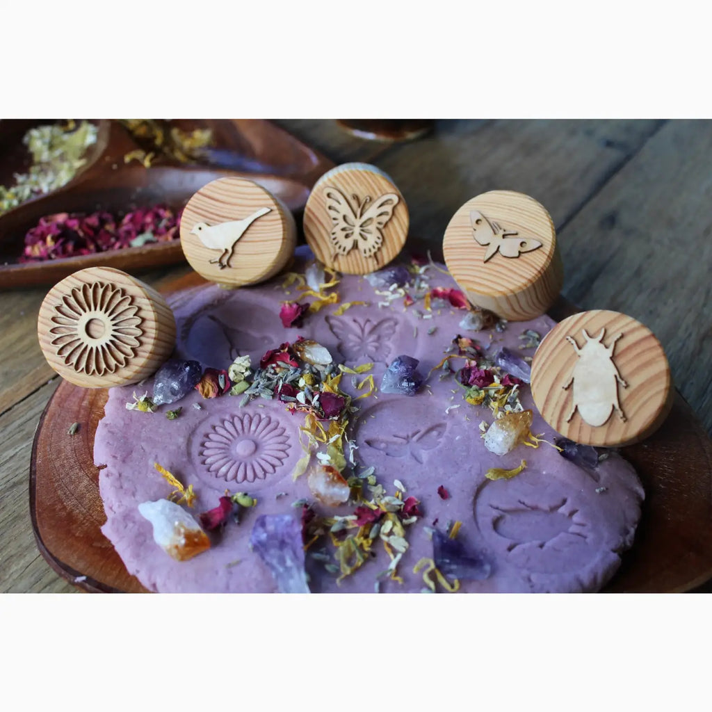 Purple clay or wax disc with flower petals and wooden stamps featuring nature designs.