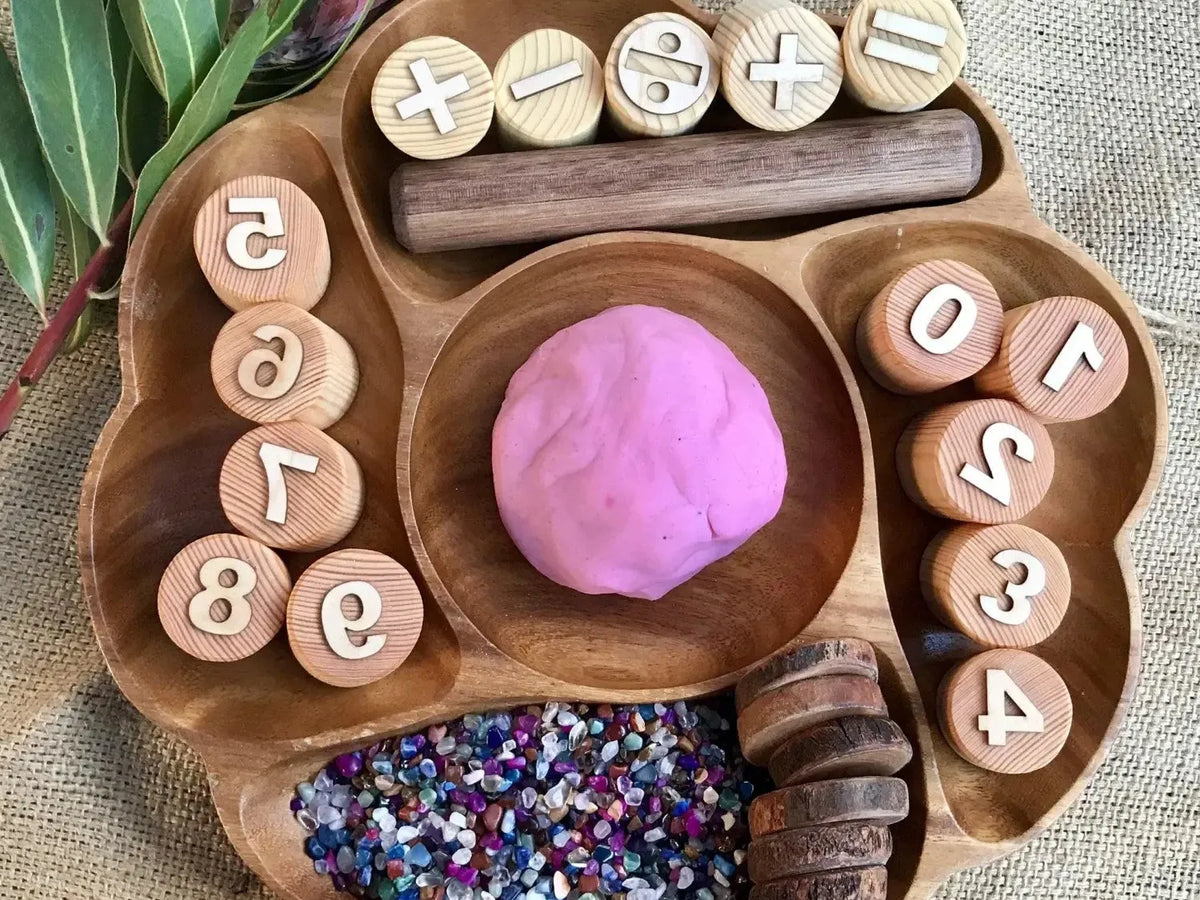 Wooden tray with compartments containing playdough, glitter, and numbered wooden discs.