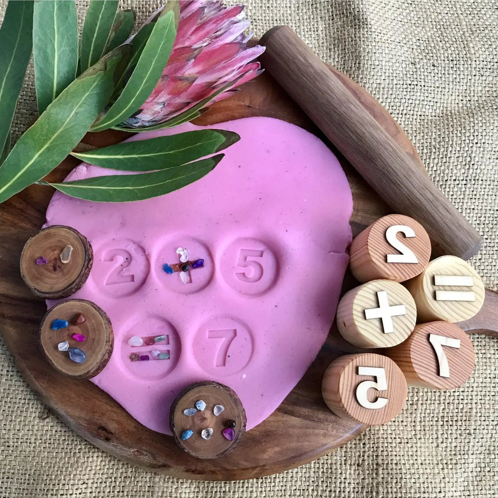 Pink heart-shaped playdough or clay with numbers and wooden discs imprinted on its surface.