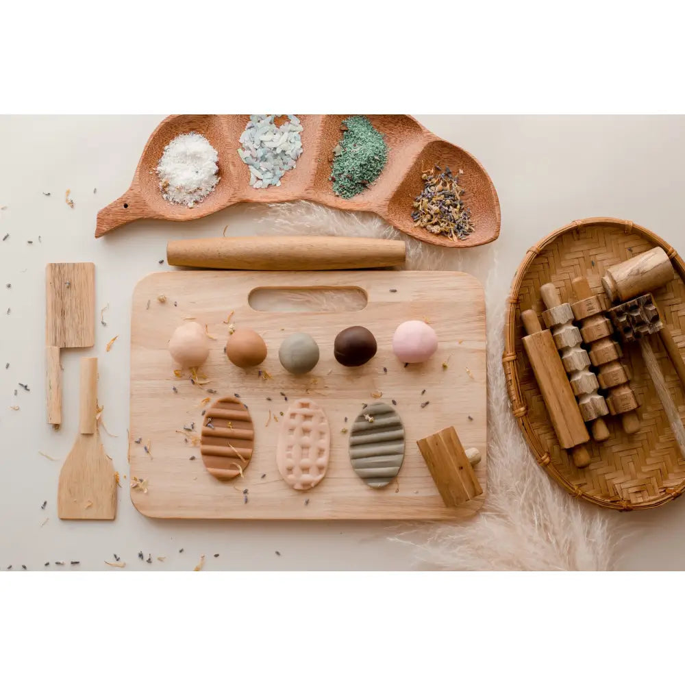 Wooden cutting board with various clay or dough shapes and tools for crafting.