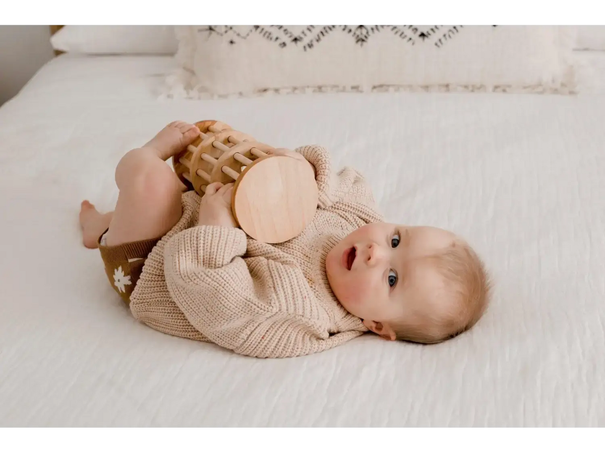 Baby lying on its back wearing a beige knit sweater.