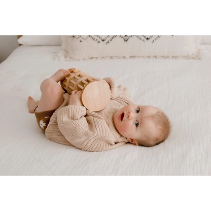 Baby lying on its back wearing a beige knit sweater.