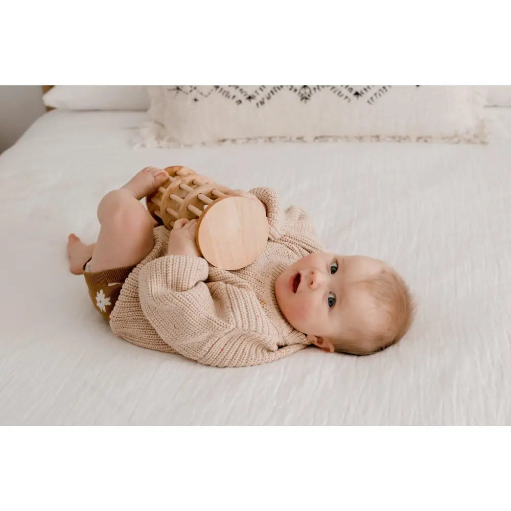 Baby lying on its back wearing a beige knit sweater.