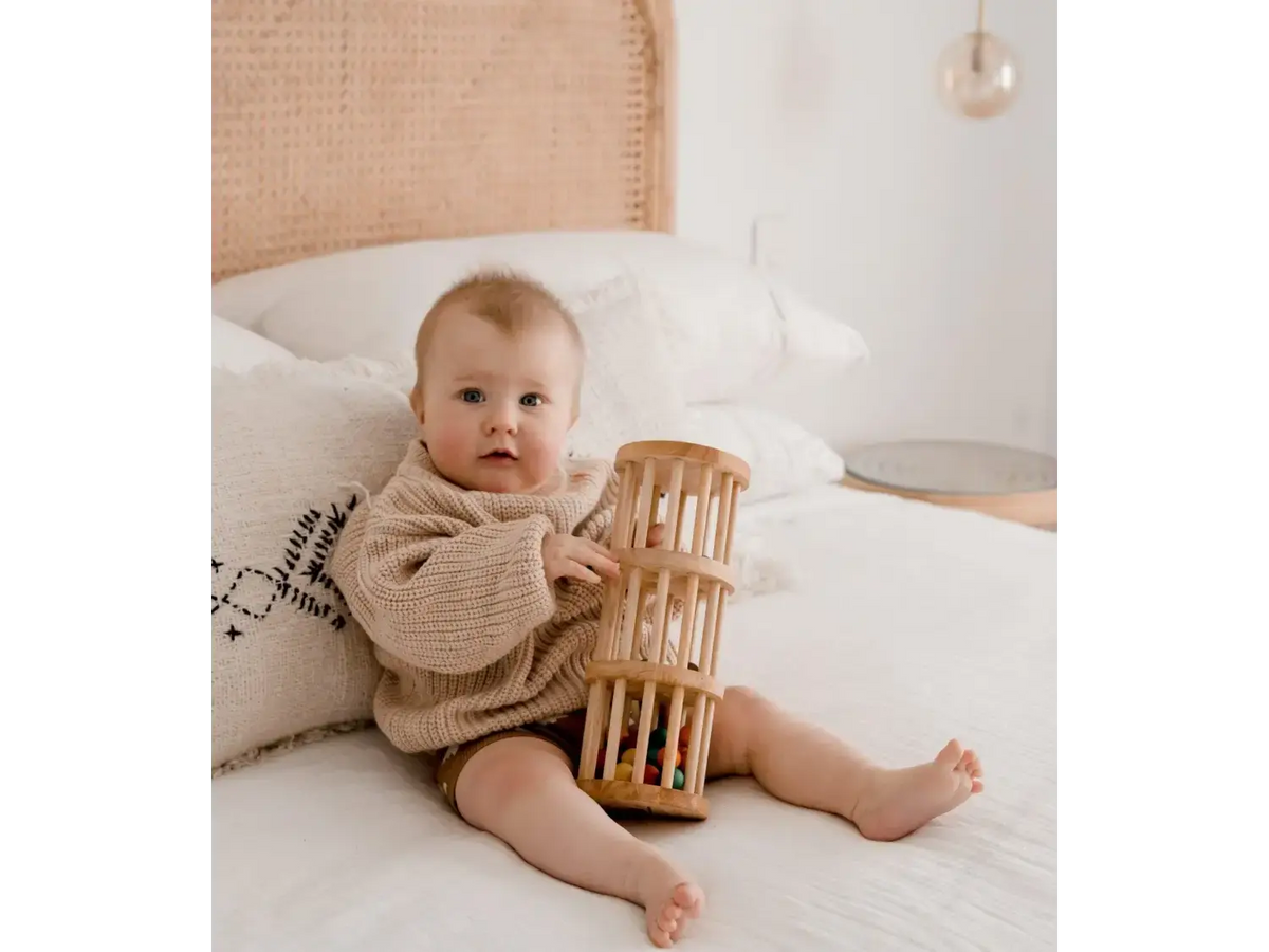 Baby sitting on a bed holding a wooden cylindrical toy.