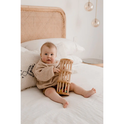 Baby sitting on a bed holding a wooden cylindrical toy.
