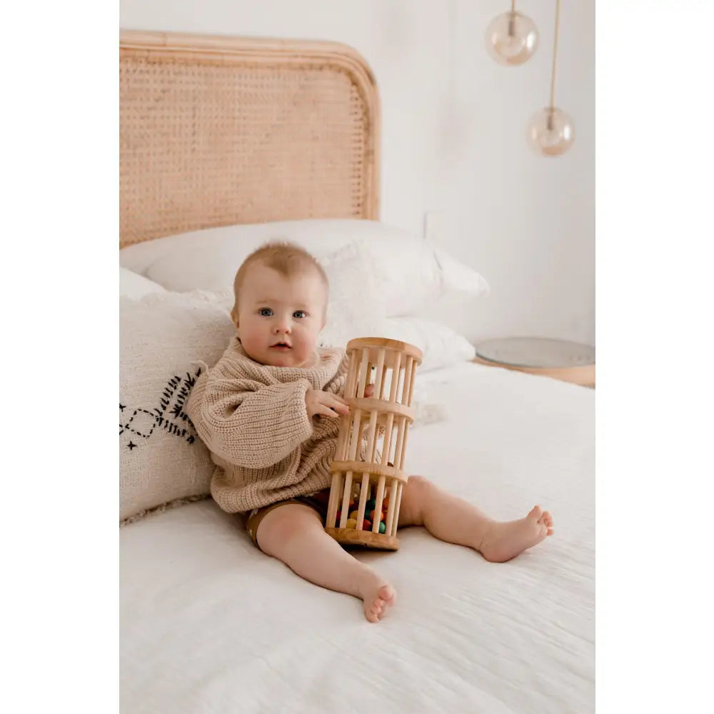 Baby sitting on a bed holding a wooden cylindrical toy.