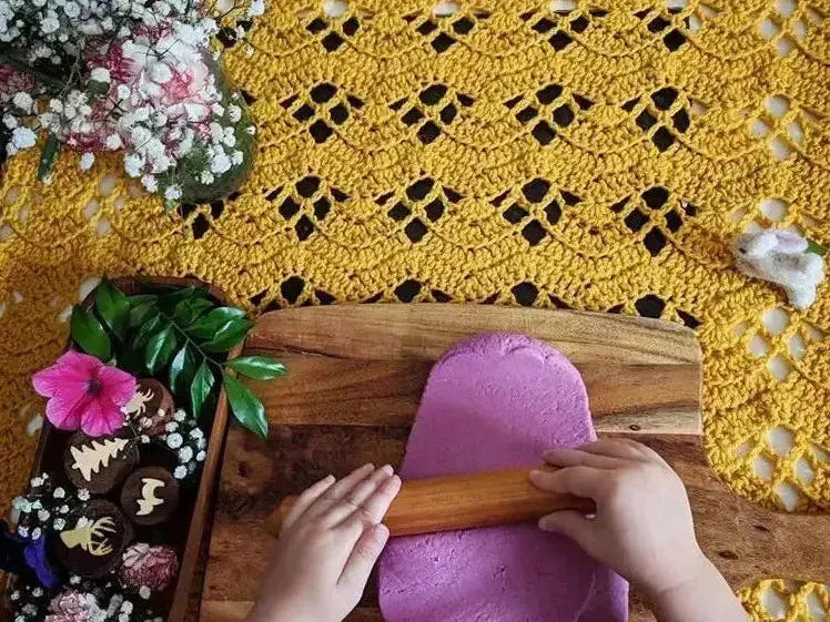 Hands kneading bright purple dough on a wooden cutting board.