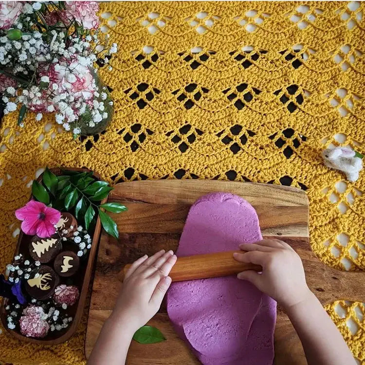 Hands kneading bright purple dough on a wooden cutting board.